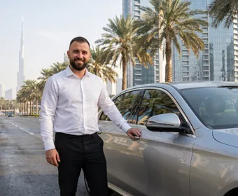 Comfort Drive driver in uniform standing beside a client's car in Dubai